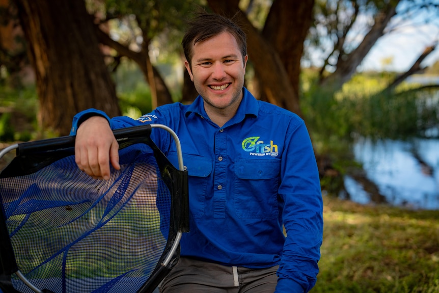 Man wearing a blue shirt sitting near a river holding a net.