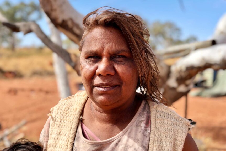 An Aboriginal woman stands smiling at the camera with the Kimberley desert in the background