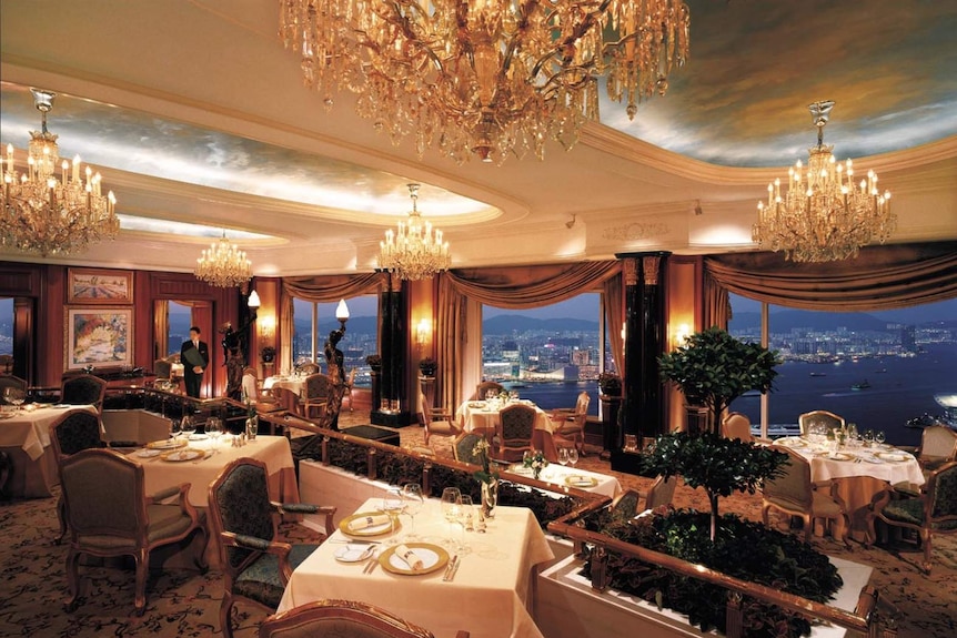 An opulent dining room with chandeliers and large windows revealing a stunning view over Hong Kong.
