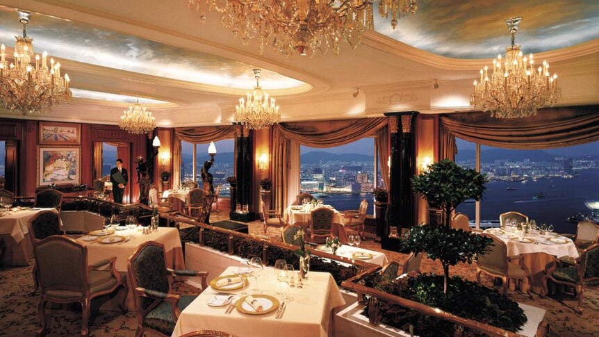 An opulent dining room with chandeliers and large windows revealing a stunning view over Hong Kong.