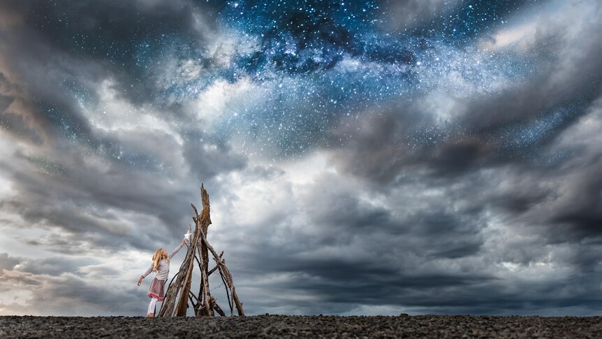 Girl placing star on driftwood tree under a starry night sky