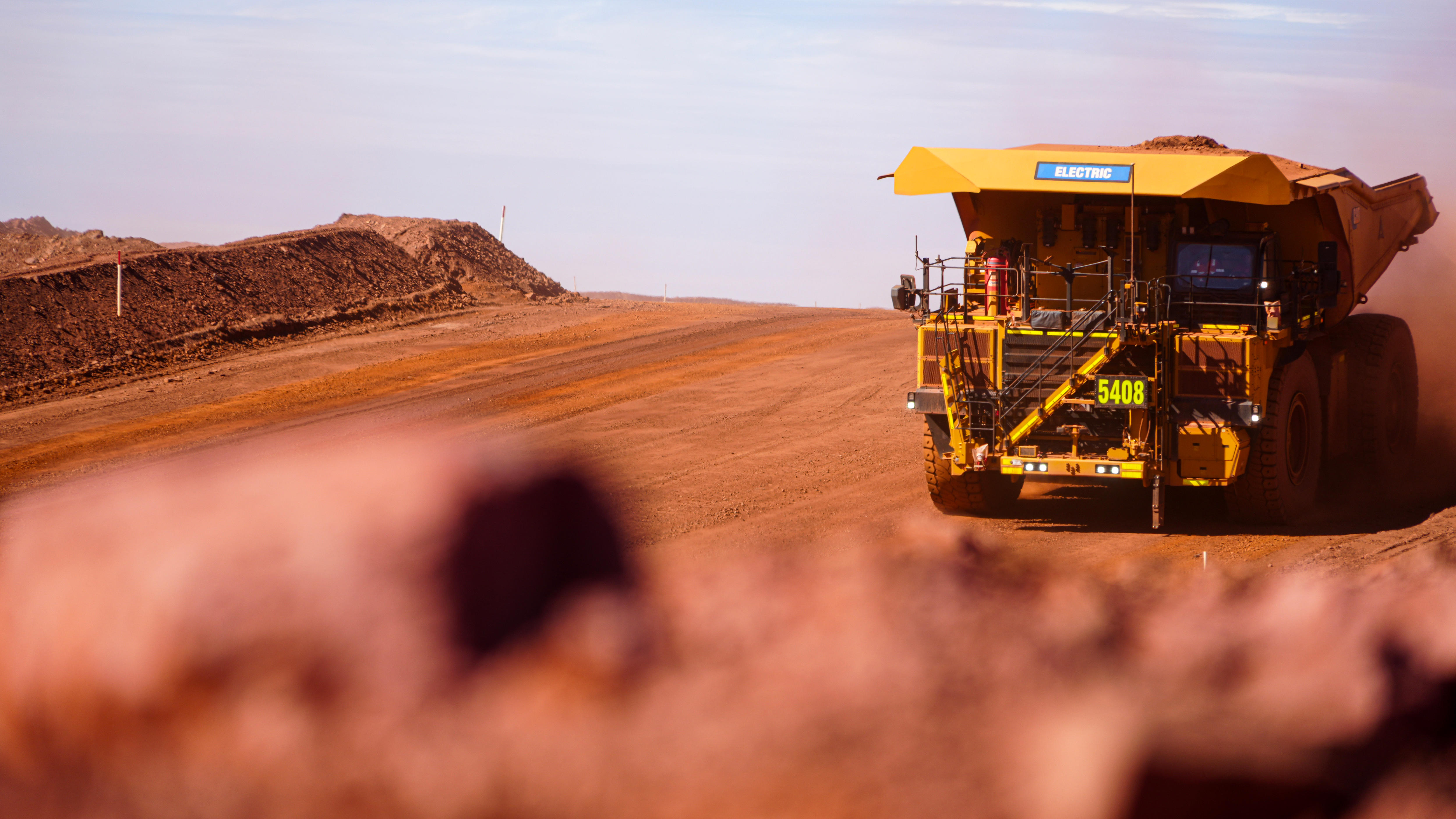 A large mining dump truck drives down a red dirt hill. 