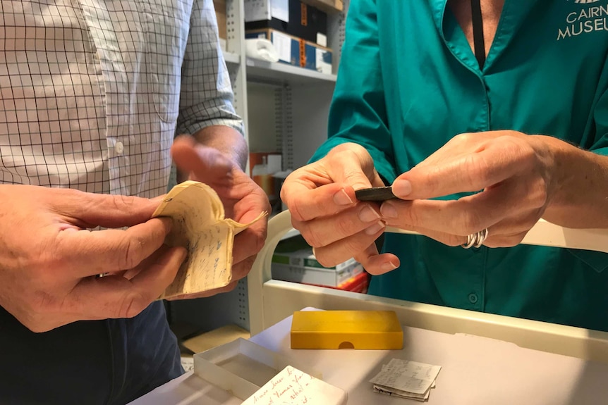 Researchers hold a bronze Ptolemaic coin in the collection library of the Cairns Museum.