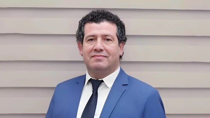 A middle-aged Palestinian man with curly dark hair in a blue suit smiles at the camera.