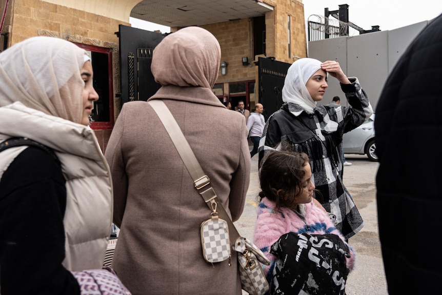A family wearing hijabs stands waiting for transport with a little girl.