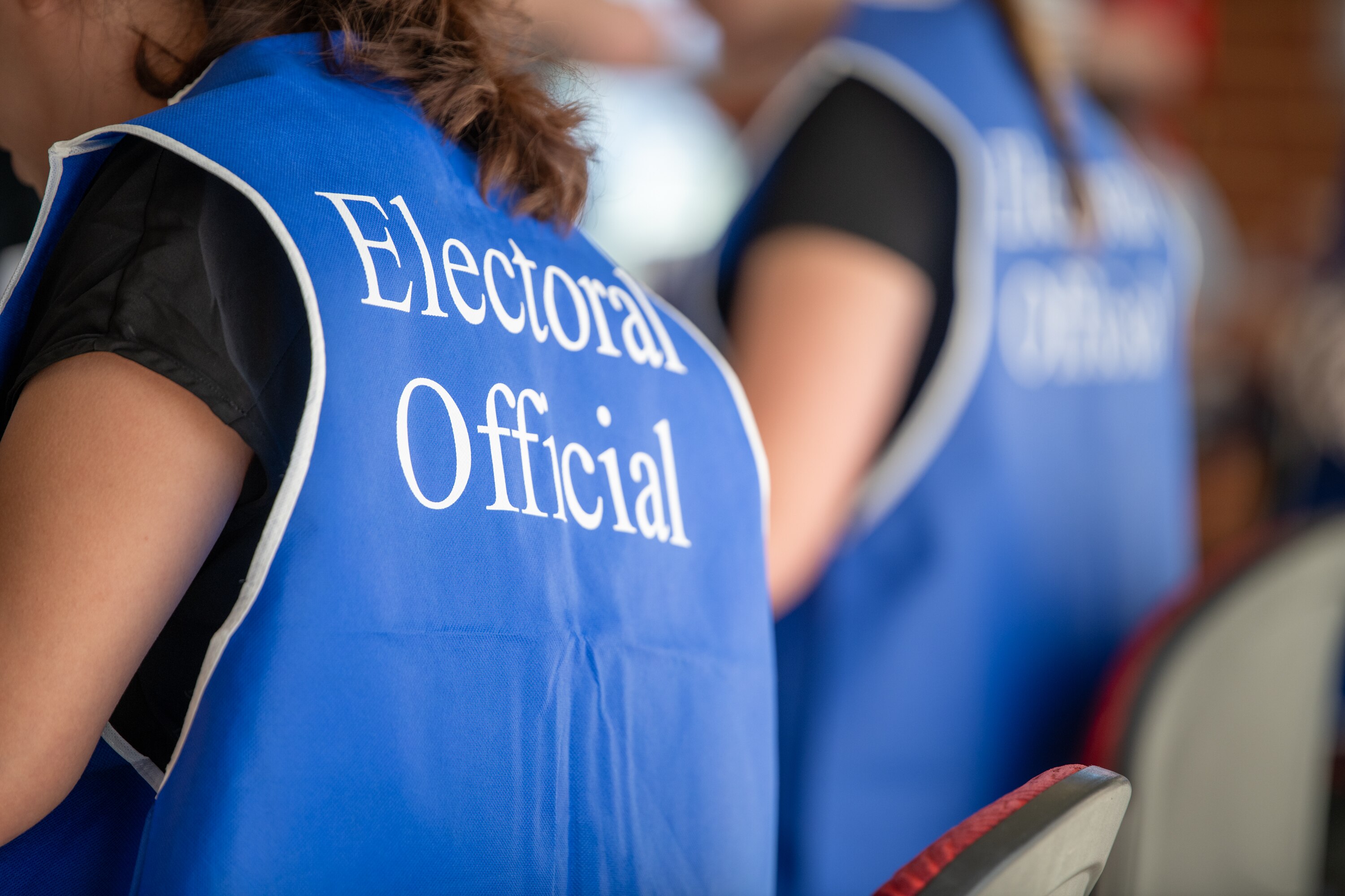 A photo taken from behind of an electoral official wearing blue vest.