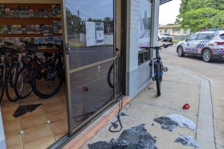 A bike shop front with broken glass on the ground out the front.