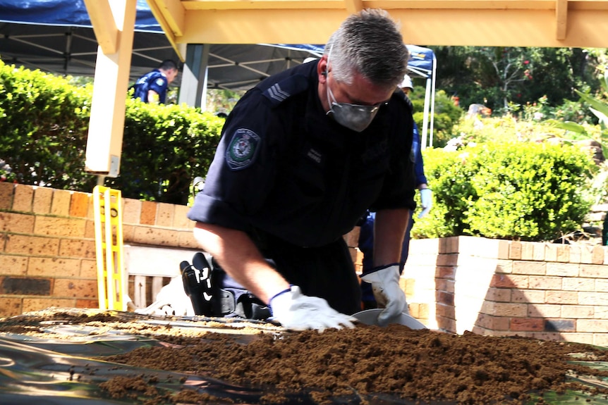 A police officer searching through dirt on a table.