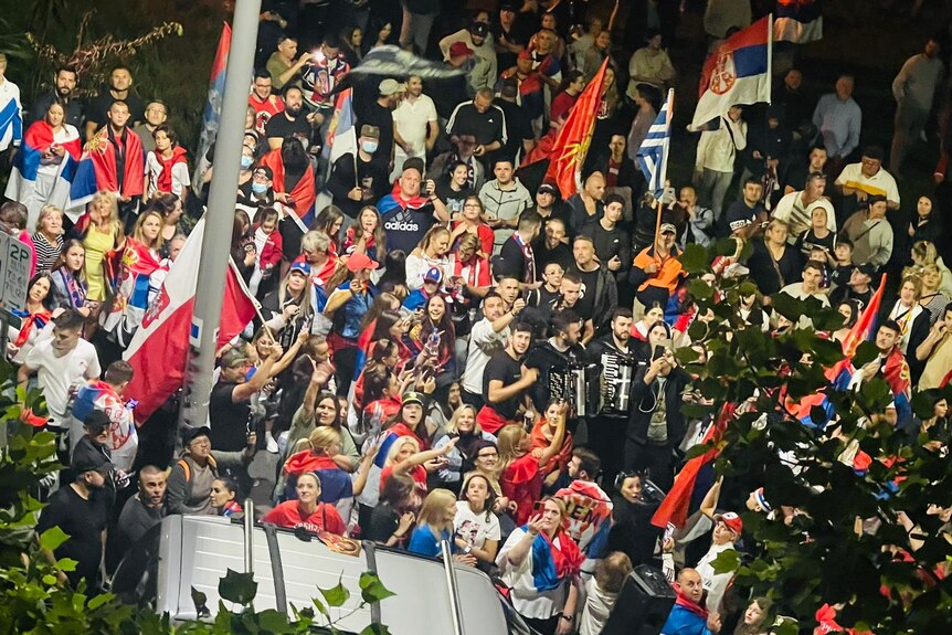 A crowd of people wave Serbian flags in the street.