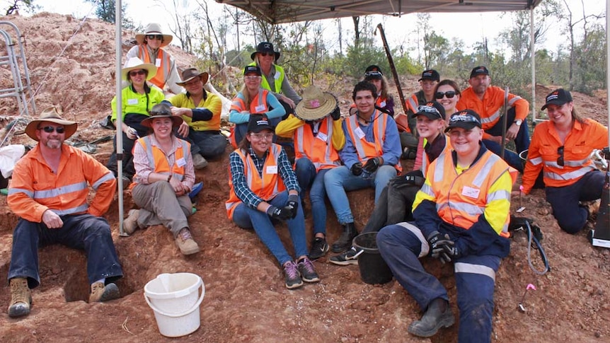 School students sitting in the dirt on a mine site smiling