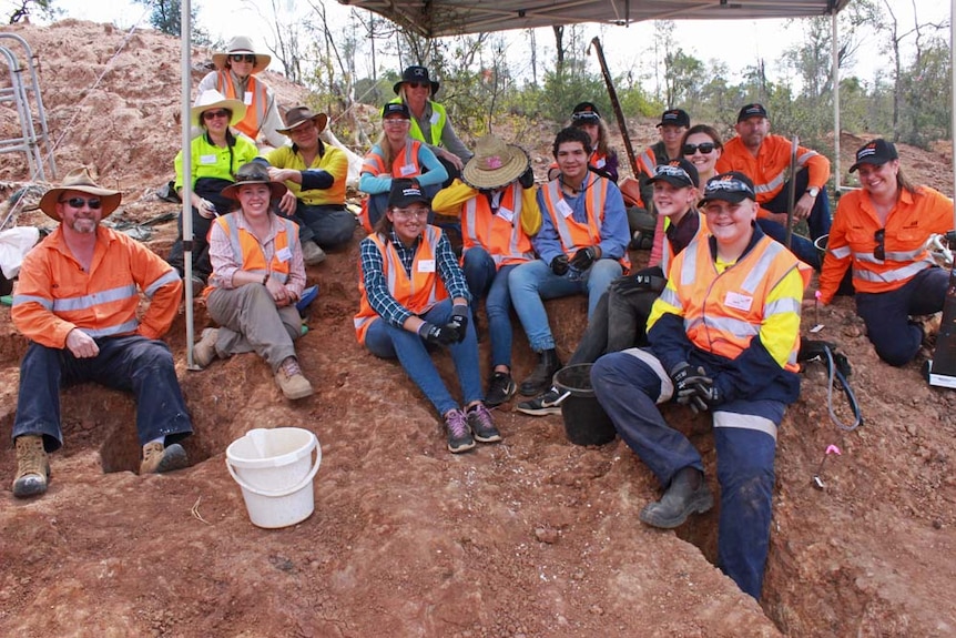 School students sitting in the dirt on a mine site smiling