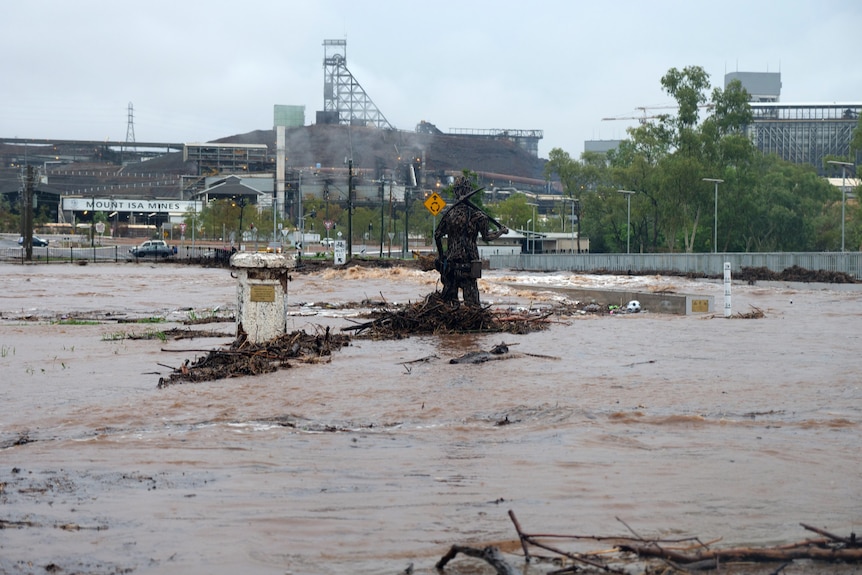 water rushing over a bridge and river debris being caught on a pillar and statue in Mount Isa