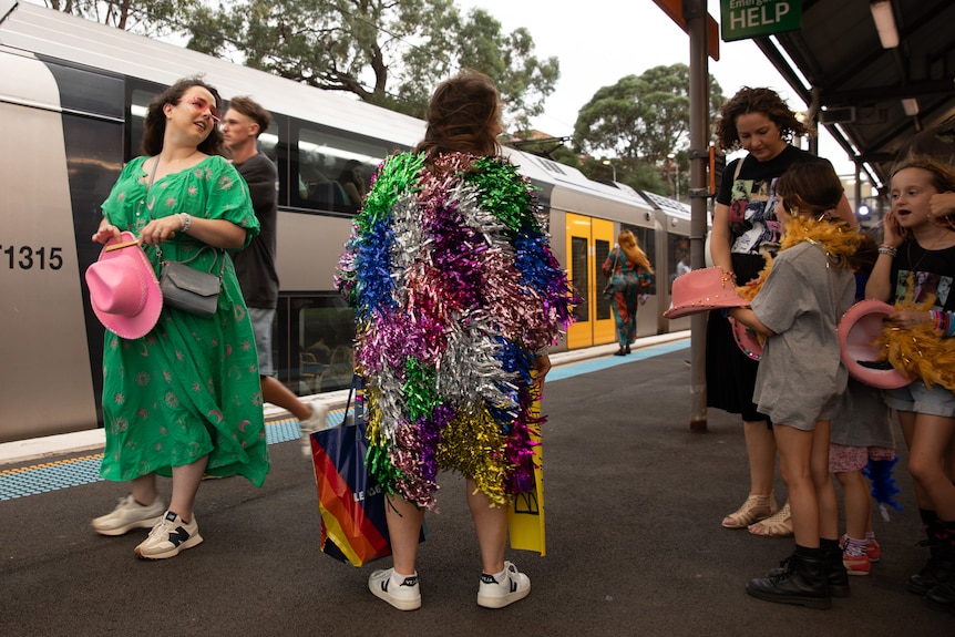A woman in a rainbow tinsel dress on an otherwise unremarkable train platform