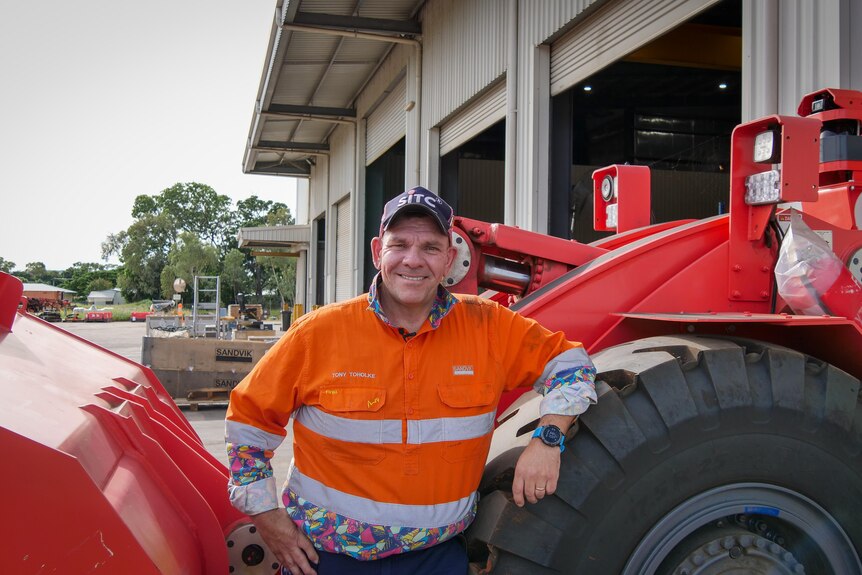 a man in hi-vis clothing smiles leaning against a truck