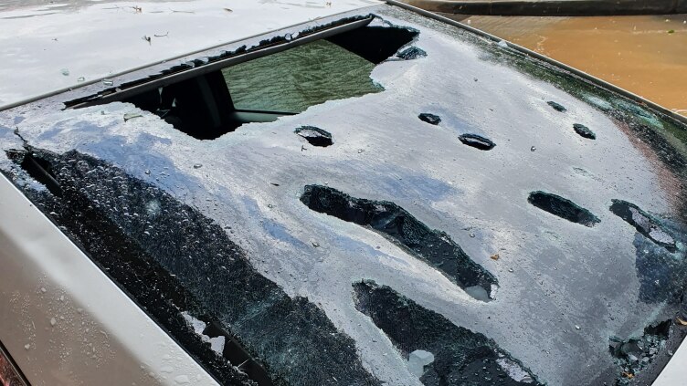 A parked car shows a windscreen smashed from hail.