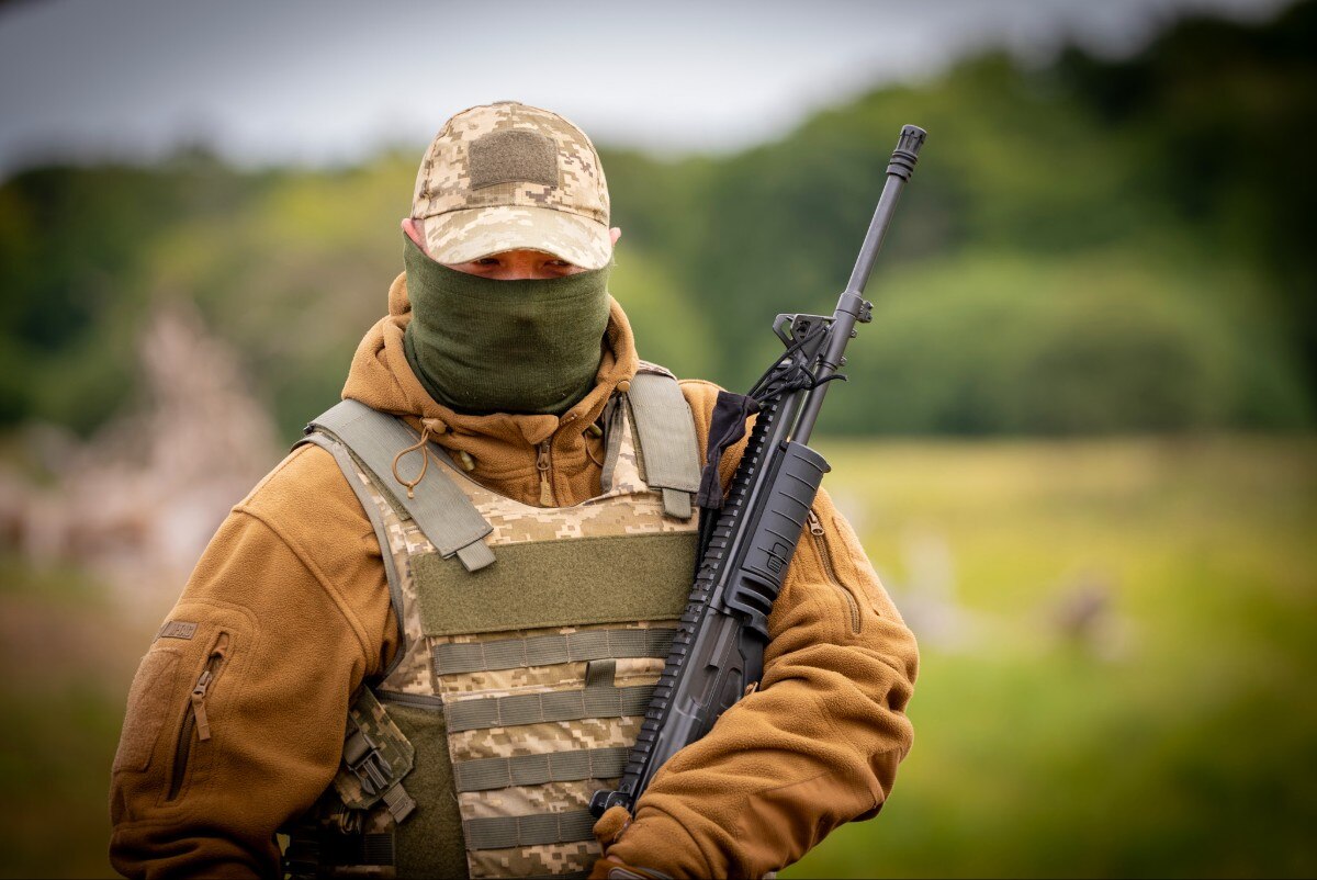 A soldier holding a gun, looking on.