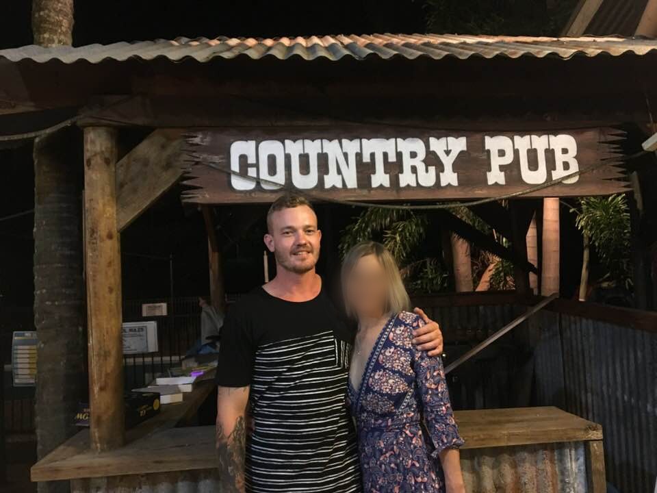 A man and woman stand together under a wooden sign with the words "country-pub".