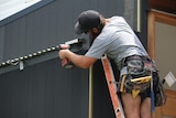 Construction worker on ladder wearing toolbelt working on a modern house in Brisbane.