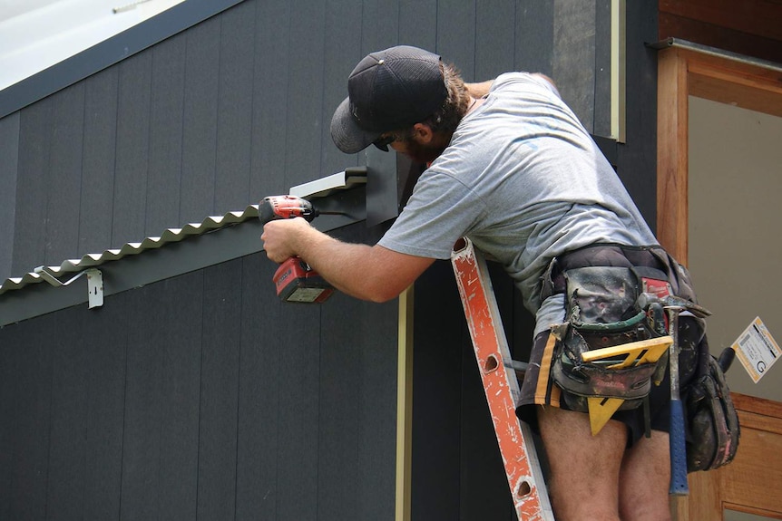 Construction worker on ladder wearing toolbelt working on a modern house in Brisbane.