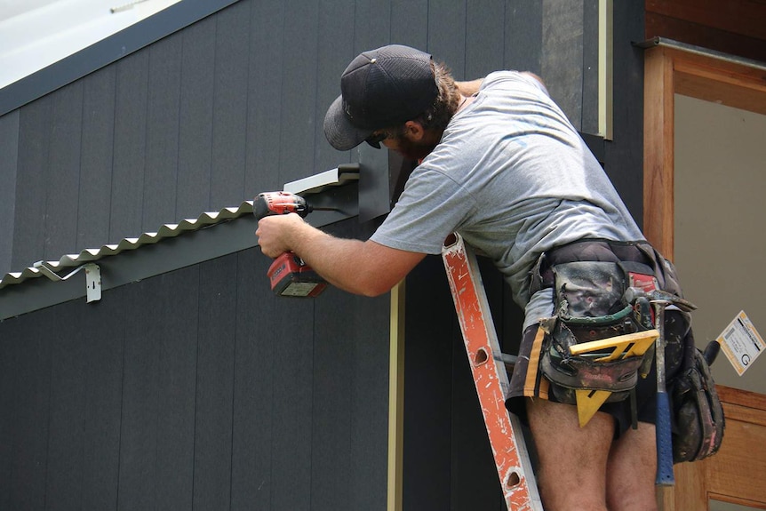 Trabajador de la construcción en una escalera con cinturón de herramientas trabajando en una casa moderna en Brisbane.