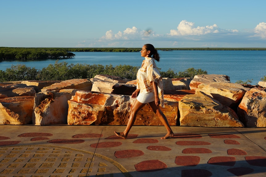 a model walks down a jetty barefoot with the ocean behind her 