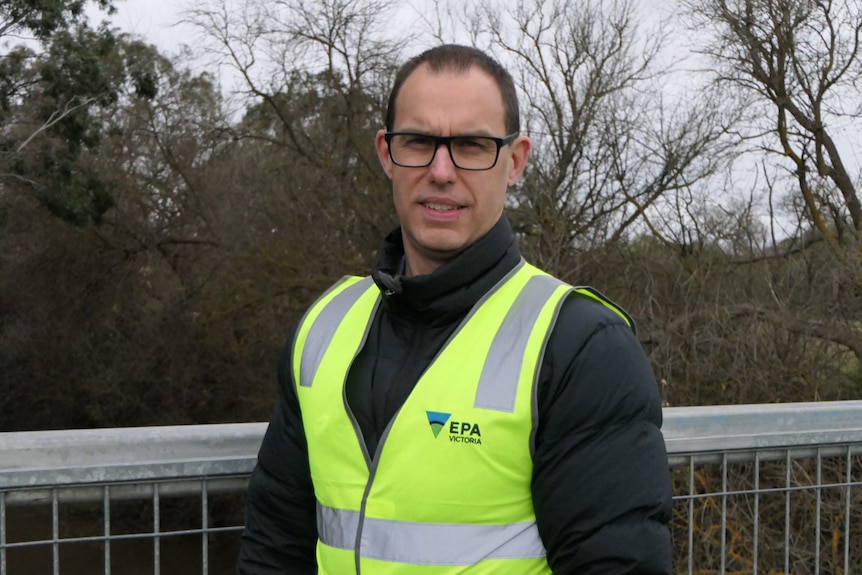 Lee Miezis stands in a high-vis vest on a bridge over the Werribee River