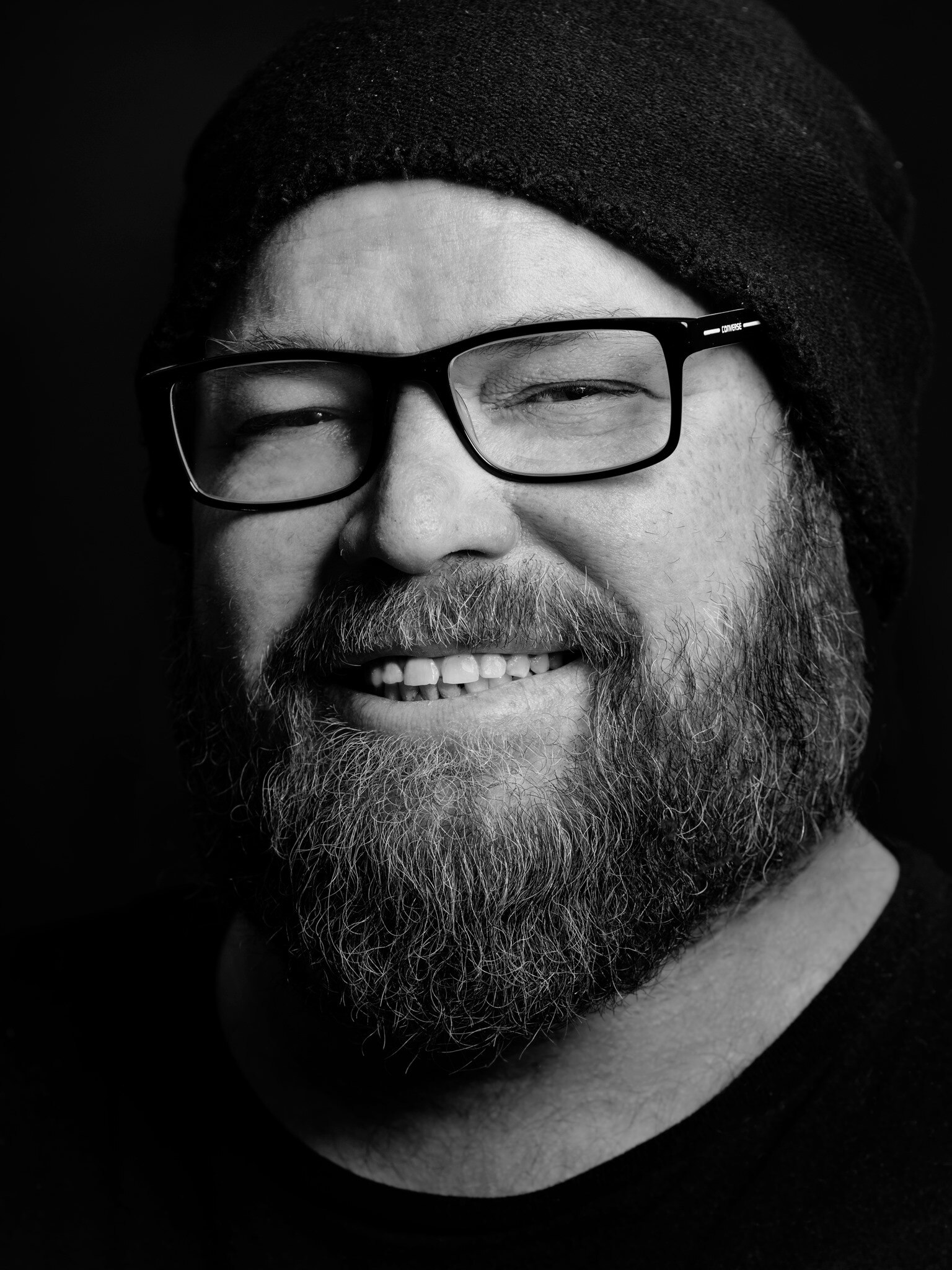 Black and white portrait of man with glasses and beard, smiling.