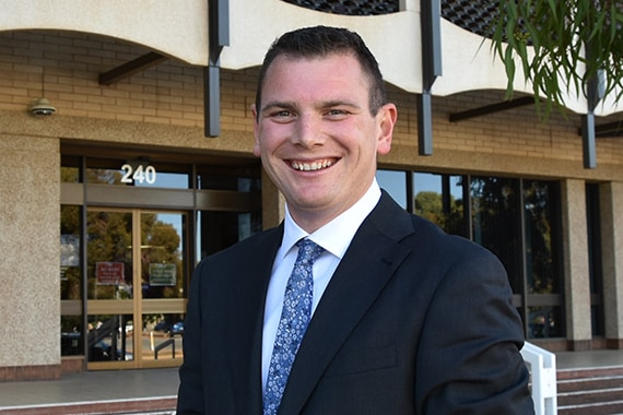 young man wearing suit smiles, standing in front of council building