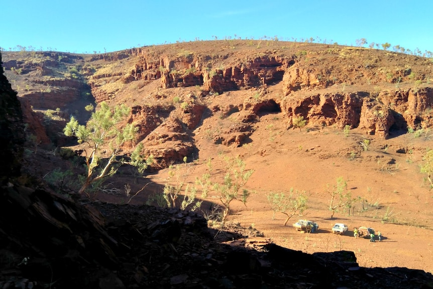 A vast red gorge pictured against a blue sky with mining workers pictured standing at the bottom.