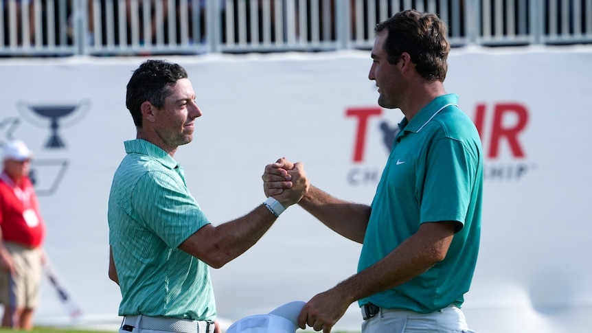 Two golfers stand on the 18th green after a big tournament, and shake hands as the man on the left wins the title.