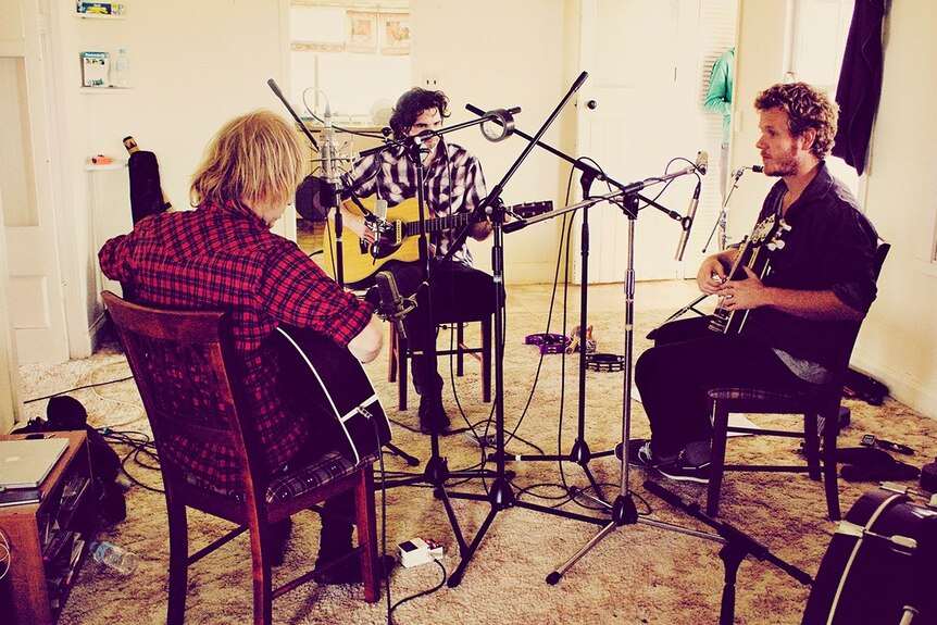 Three musicians playing guitars and recording music in a house.