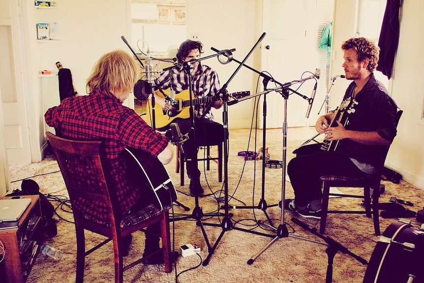 Three musicians playing guitars and recording music in a house.