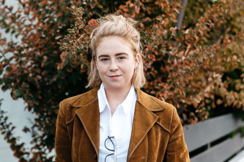 Abbey Kendall stands in front of a park bench and a tree.