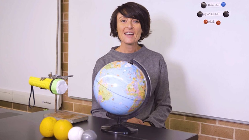 Female teacher sits with globe of Earth