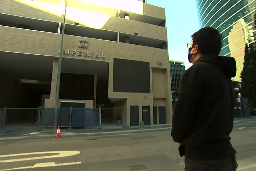 A man wearing a mask stands outside the Imperial Towers complex in Parramatta.