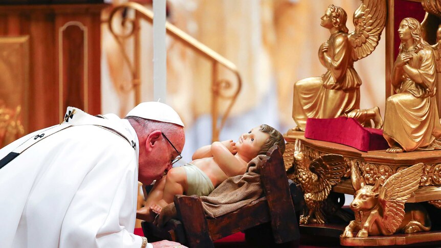 Pope Francis kisses a statue of baby Jesus.