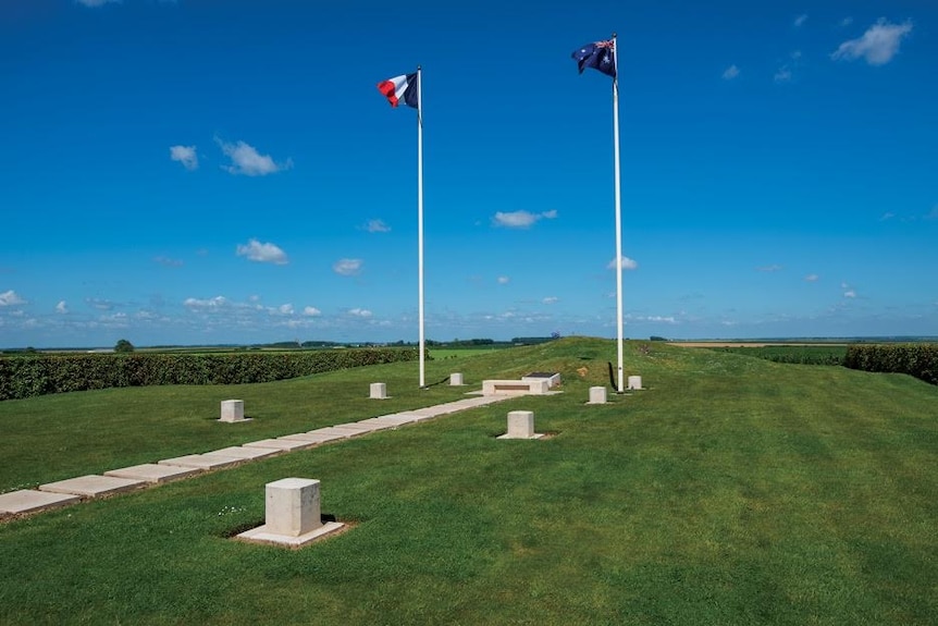 Two flag poles with French and Australian flags flying in a grassy field in Pozieres