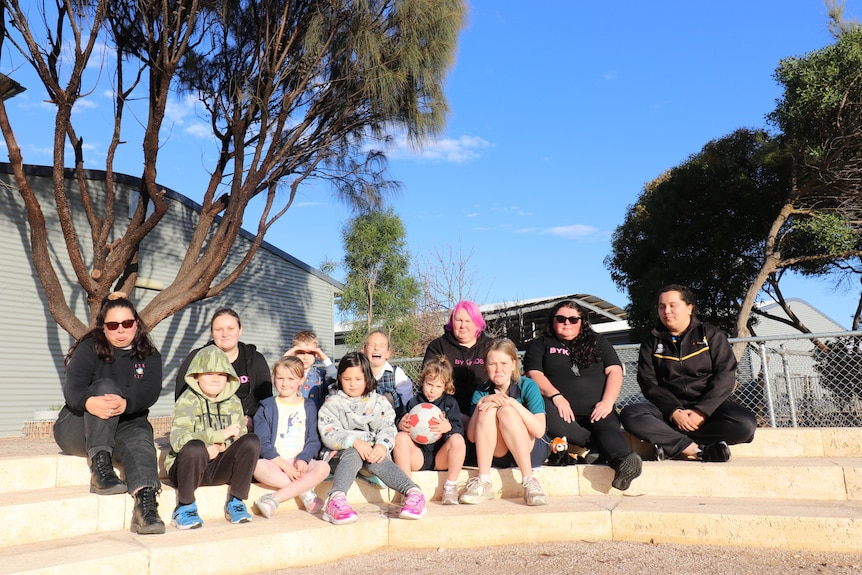 A photo of care provider staff and children sitting down looking sad.