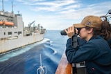 A female US naval officer looks at another vessel through a range finder.