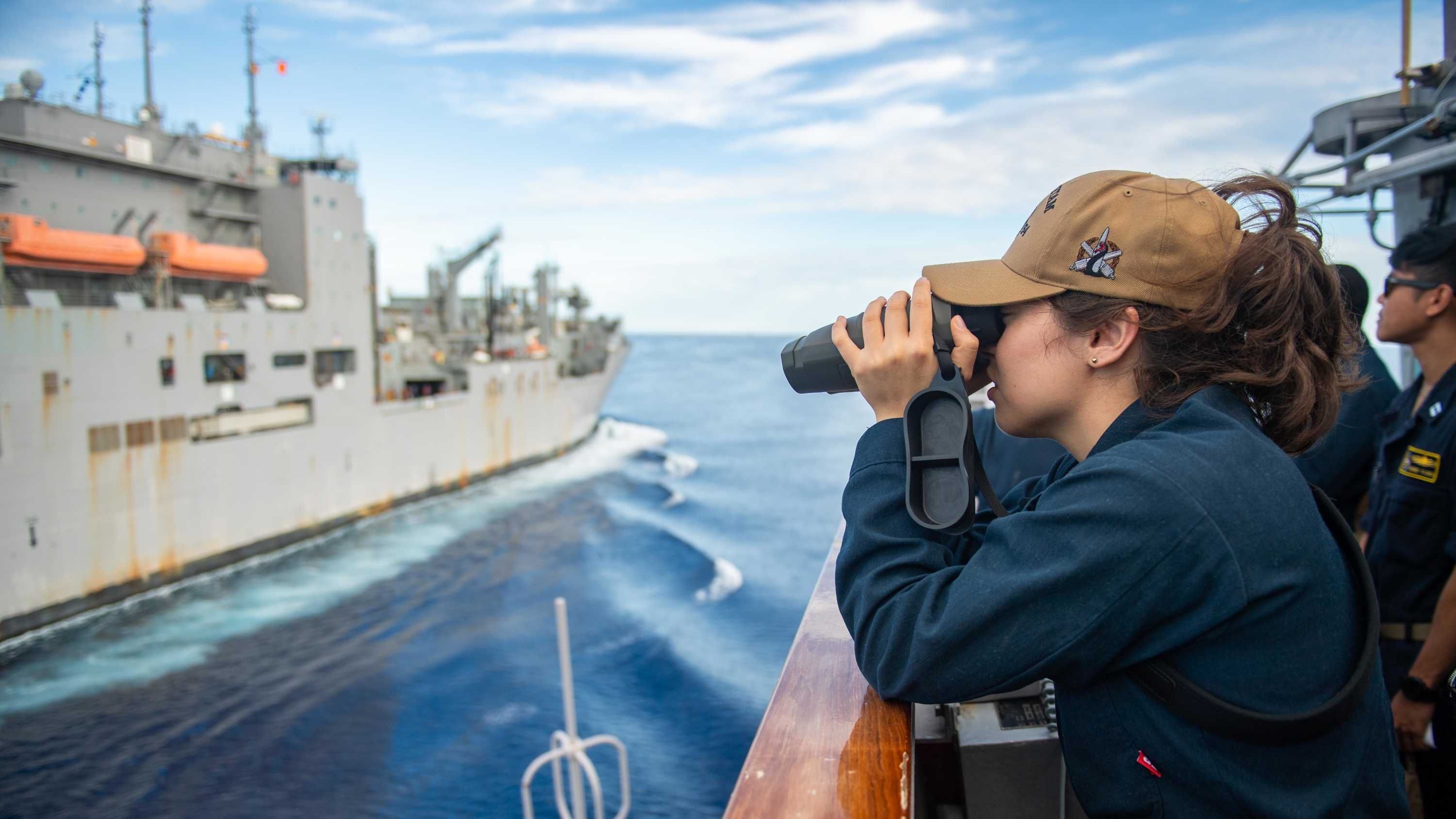 一名女海军军官看着另一艘船通过测距仪。” class=