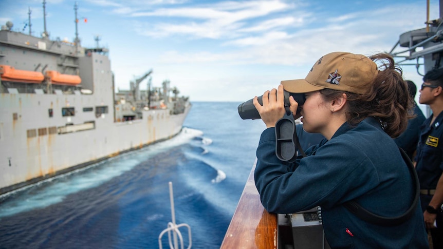 A female naval officer looks at another vessel through a range finder.