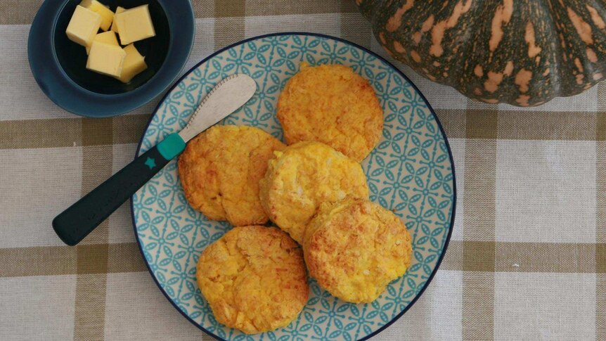 Scones on a plate with a whole pumpkin and a bowl of butter next to it.