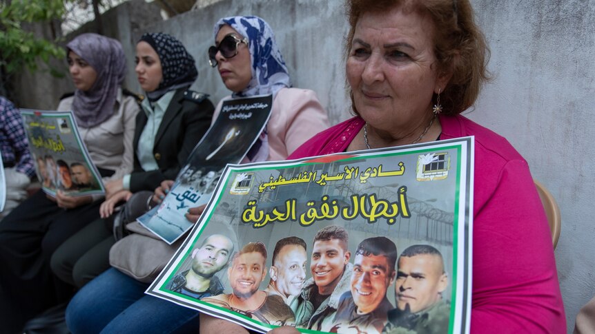 A woman holds a printed poster showing six Palestinian men with Arabic writing.