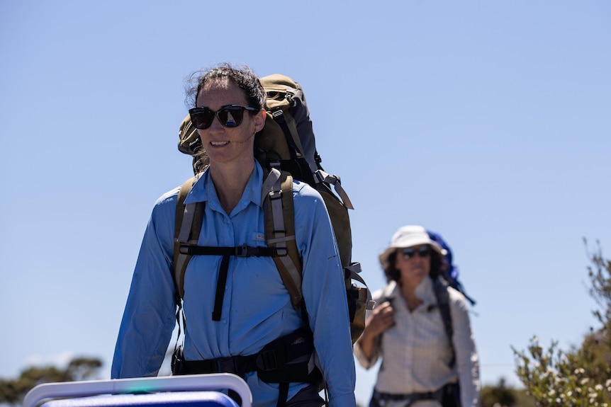 Two women wearing hiking backpacks walk towards the camera
