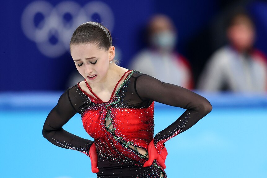 An emotional female figure skater looks down at the ice with her hands on her hips after her final Winter Olympic skate. 