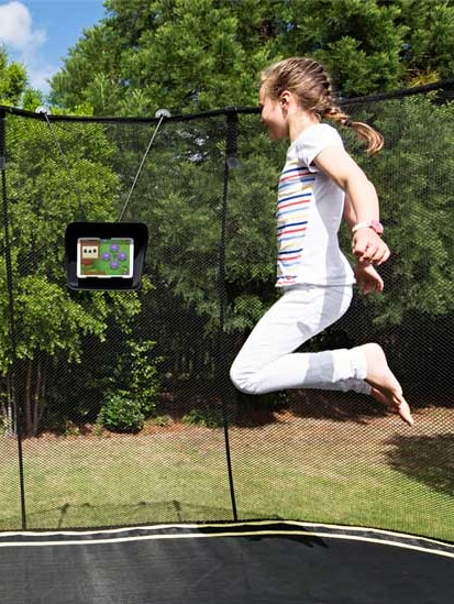 Girl jumping on Smart Trampoline while looking at a tablet.
