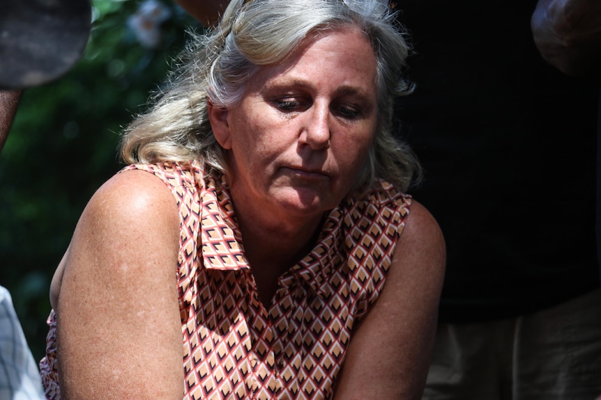 A close-up of a woman with grey hair, wearing a short-sleeved blouse