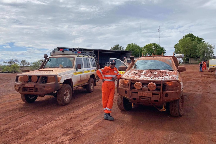 An SES volunteer poses with two very dirty four wheel drive vehicles