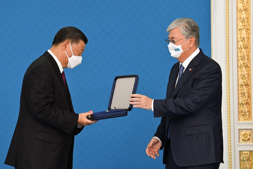 A man in a dark suit with grey hair wearing a mask presents Xi Jinping with a black box.