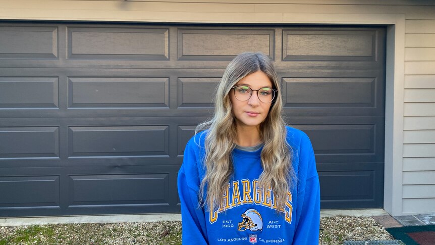 A young woman in a blue jumper in front of a garage door